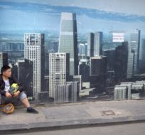 A worker sits in front of a billboard at a construction site in Beijing. Mark Schiefelbein/AP Photo.