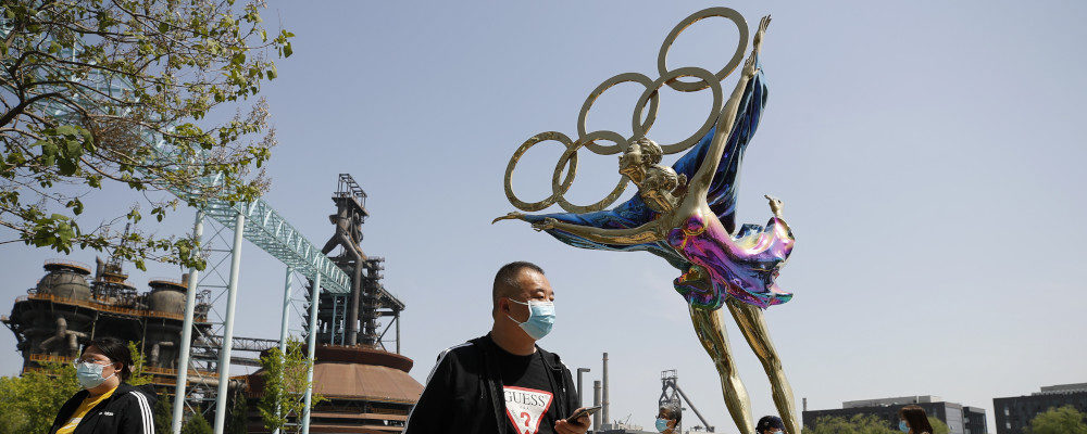 Visitors wearing face masks to help curb the spread of the coronavirus walk by a statue featuring Winter Olympics figure skating on display at the Shougang Park in Beijing on May 2, 2021. Andy Wong/AP Photo.
