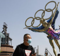 Visitors wearing face masks to help curb the spread of the coronavirus walk by a statue featuring Winter Olympics figure skating on display at the Shougang Park in Beijing on May 2, 2021. Andy Wong/AP Photo.