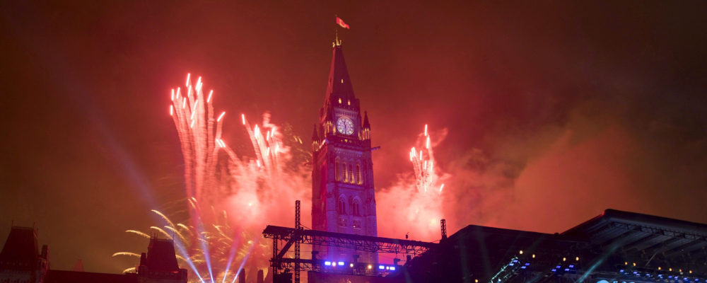 People wearing Canadian flags watch fireworks explode during the evening ceremonies of Canada's 150th anniversary of Confederation, in Ottawa on July 1, 2017. Justin Tang/The Canadian Press.