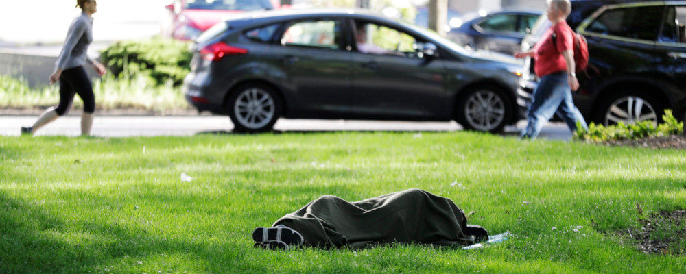 In this Monday, May 7, 2018, photo, a person sleeps under a blanket on the grass at Denny Park in Seattle, not far from Amazon.com's headquarters. Ted S. Warren/AP Photo.