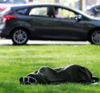 In this Monday, May 7, 2018, photo, a person sleeps under a blanket on the grass at Denny Park in Seattle, not far from Amazon.com's headquarters. Ted S. Warren/AP Photo.