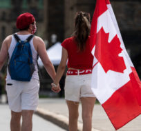 People hold a Canadian flag as they walk on Parliament Hill in Ottawa on Canada Day, Thursday, July 1, 2021. Justin Tang/THE CANADIAN PRESS.