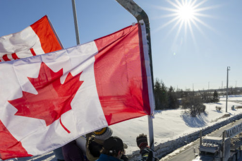 Supporters wave flags on an overpass in Kanata, Ont., as a trucker convoy making it's way to Parliament Hill in Ottawa. Frank Gunn/The Canadian Press.