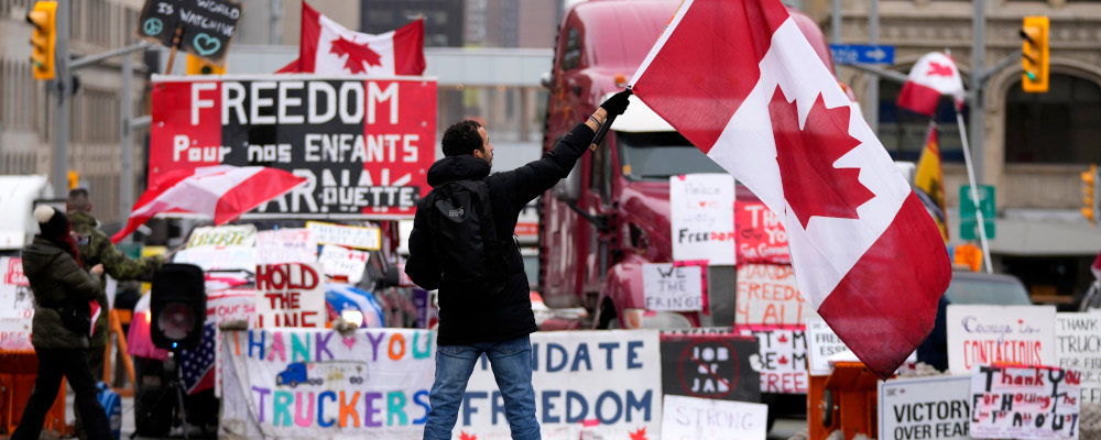 A protester waves a Canadian flag in front of parked vehicles on Rideau Street on the 15th day of a protest against COVID-19 measures that has grown into a broader anti-government protest, in Ottawa, Friday, Feb. 11, 2022. Justin Tang/The Canadian Press. 