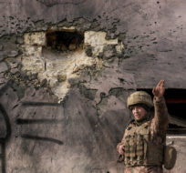 A Ukrainian serviceman points to the direction of the incoming shelling next to a building which was hit by a large caliber mortar shell in the frontline village of Krymske, Luhansk region, in eastern Ukraine, Saturday, Feb. 19, 2022. Vadim Ghirda/AP Photo.