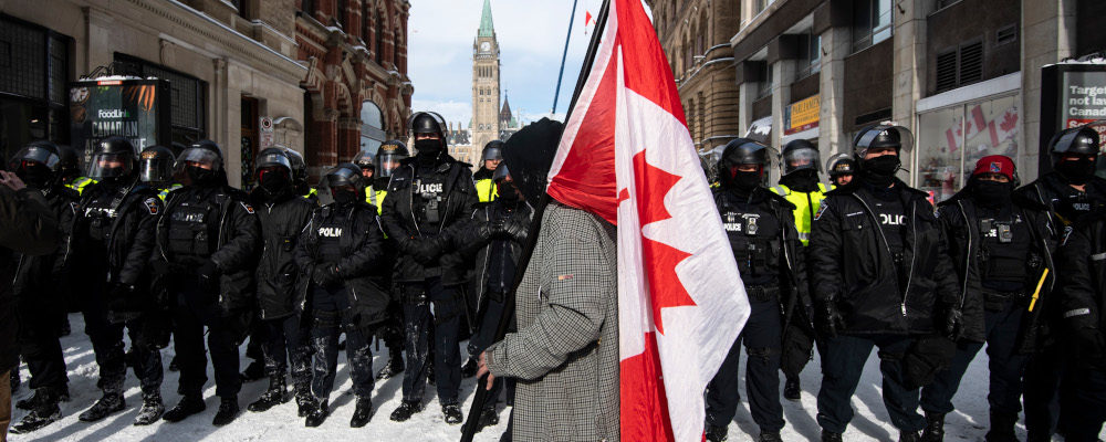 A protester walks with a Canadian flag as police move in to clear downtown Ottawa near Parliament Hill of protesters after weeks of demonstrations on Saturday, Feb. 19, 2022. Justin Tang/The Canadian Press.