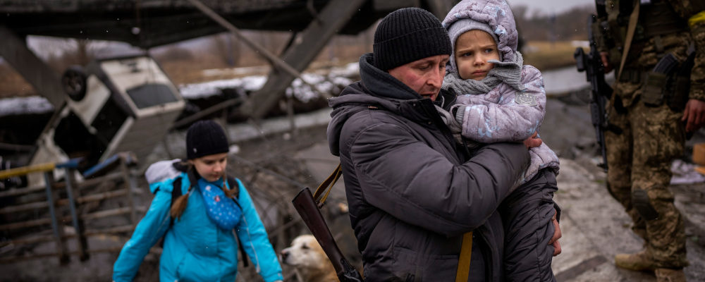 Local militiaman Valery, 37, carries a child as he helps a fleeing family across a bridge destroyed by artillery, on the outskirts of Kyiv, Ukraine, Wednesday, March 2. 2022. Russian forces have escalated their attacks on crowded cities in what Ukraine's leader called a blatant campaign of terror. Emilio Morenatti/AP Photo.