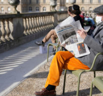 A man wearing face mask, reads Le Monde newspaper in the Luxembourg garden next the French Senate building seeing in background, in Paris, France, Monday, March 14, 2022. Francois Mori/AP Photo.