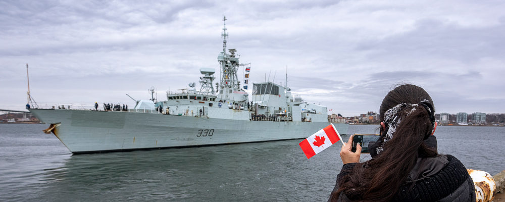 A woman takes a photo as HMCS Halifax departs Halifax in support of NATO's deterrence measures in eastern Europe on Saturday, March 19, 2022. Andrew Vaughan/The Canadian Press.
