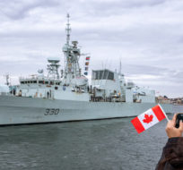A woman takes a photo as HMCS Halifax departs Halifax in support of NATO's deterrence measures in eastern Europe on Saturday, March 19, 2022. Andrew Vaughan/The Canadian Press.