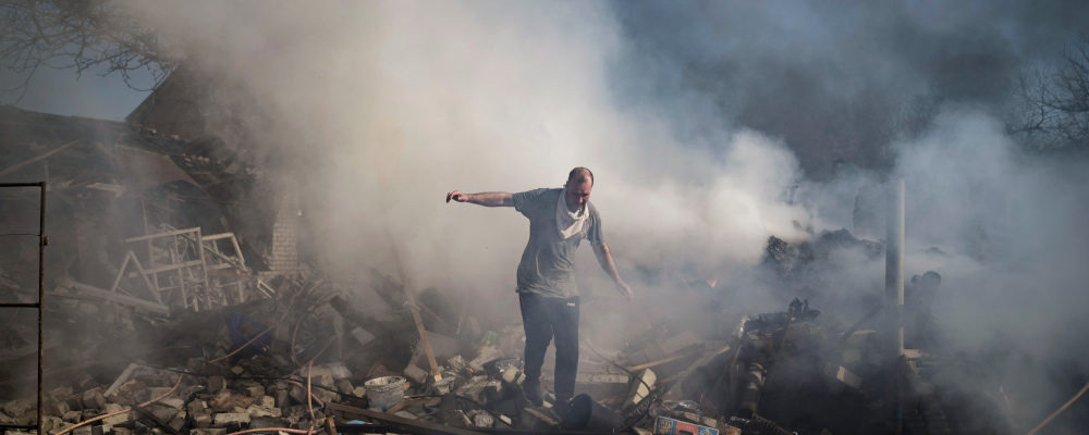 A neighbour walks on the debris of a burning house, destroyed after a Russian attack in Kharkiv, Ukraine, Thursday, March 24, 2022. Felipe Dana/AP Photo.