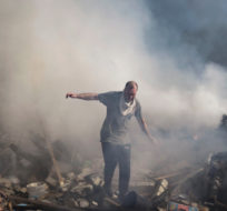 A neighbour walks on the debris of a burning house, destroyed after a Russian attack in Kharkiv, Ukraine, Thursday, March 24, 2022. Felipe Dana/AP Photo.