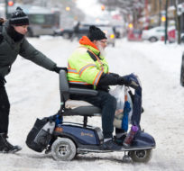Pedestrians help a man in a motorized wheelchair across a snowy street in downtown Vancouver, B.C., Wednesday, January 15, 2020. Jonathan Hayward/The Canadian Press.