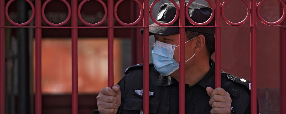 A security guard wearing a mask to help protect from the coronavirus stands behind a fence, Monday, March 28, 2022, in Beijing. China began its largest lockdown in two years Monday to conduct mass testing and control a growing outbreak in its largest city of Shanghai as questions are raised about the economic toll of the nation's "zero-COVID" strategy. Andy Wong/AP Photo.