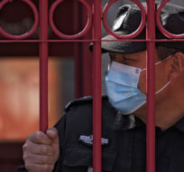 A security guard wearing a mask to help protect from the coronavirus stands behind a fence, Monday, March 28, 2022, in Beijing. China began its largest lockdown in two years Monday to conduct mass testing and control a growing outbreak in its largest city of Shanghai as questions are raised about the economic toll of the nation's "zero-COVID" strategy. Andy Wong/AP Photo.