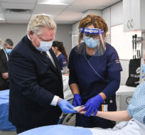 Ontario Premier Doug Ford, left, is shown how to properly check the pulse of nursing student Sofiia Daysh, right, by student Ugochinyere Ezeh, centre, as he tours a mock up health-care unit that have second year nursing students working on high fidelity simulators at Humber College during the COVID-19 pandemic in Toronto on Tuesday, March 16, 2021. Nathan Denette/The Canadian Press.