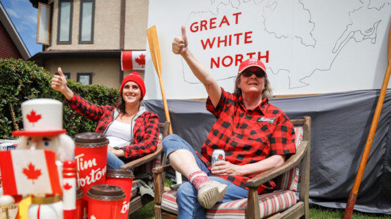 Linda Myers and her daughter Riley Myers wave to cars from in front of their Canada Day decorated house on Canada Day in Airdrie, Alta., Wednesday, July 1, 2020. Jeff McIntosh/The Canadian Press.