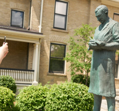 Allison Mimlos takes a photograph of a statue of Sir Frederick Banting at Banting House National Historic Site in London, Ont., on June 29, 2019. Geoff Robins/The Canadian Press.