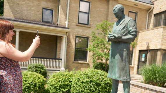 Allison Mimlos takes a photograph of a statue of Sir Frederick Banting at Banting House National Historic Site in London, Ont., on June 29, 2019. Geoff Robins/The Canadian Press.