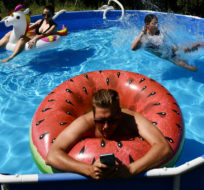 Barnabas types on his phone as he works from the home office as a pool in the garden while his wife, Rebeka, left and sister-in-law, Emma, cool down in Budapest, Hungary, Thursday, Aug. 4, 2022. Anna Szilagyi/AP Photo.