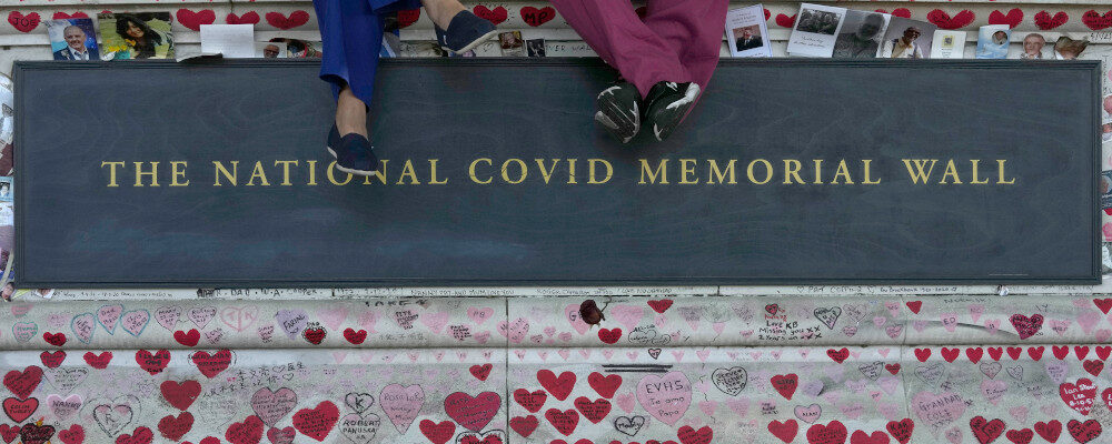 Members of the NHS staff of the nearby St Thomas Hospital enjoy their lunch break sitting in the shade on the National Covid Memorial Wall in London, Thursday, Aug. 11, 2022. Frank Augstein/AP Photo.