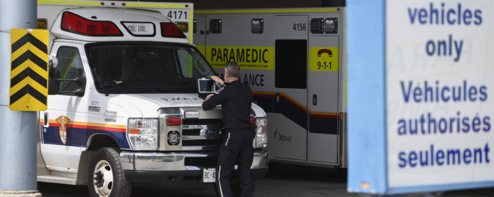 A paramedic works on a laptop on the hood of their ambulance, outside the Emergency Department at the Ottawa Hospital Civic Campus in Ottawa on May 16, 2022. Justin Tang/The Canadian Press.