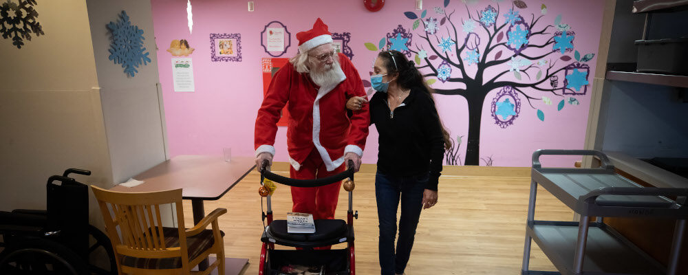 Inglewood Care Centre resident Terry Clarke, left, who likes to dress up as Santa during the holiday season, is helped by a recreational therapist at a long-term care home, in West Vancouver, on Thursday, December 16, 2021. Darryl Dyck/The Canadian Press.