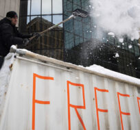 A trucker shovels snow off the top of a big rig's trailer as they prepare to drive away after participating in a blockade on Metcalfe Street, as police begin clearing the streets near Parliament Hill to end to a protest in Ottawa, Saturday, Feb. 19, 2022. Justin Tang/The Canadian Press.