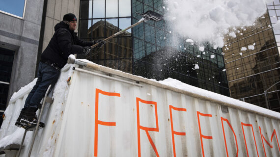 A trucker shovels snow off the top of a big rig's trailer as they prepare to drive away after participating in a blockade on Metcalfe Street, as police begin clearing the streets near Parliament Hill to end to a protest in Ottawa, Saturday, Feb. 19, 2022. Justin Tang/The Canadian Press.