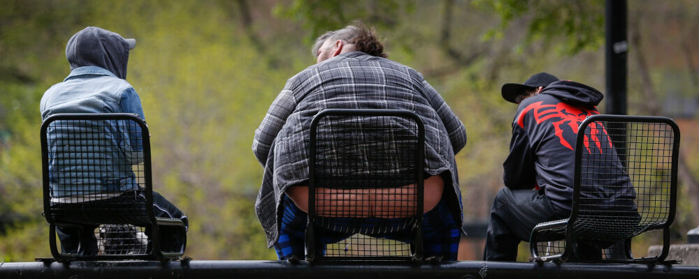 An obese man sits on a park bench with two others in Calgary, Alta., Monday, May 17, 2021. Jeff McIntosh/The Canadian Press. 