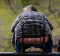 An obese man sits on a park bench with two others in Calgary, Alta., Monday, May 17, 2021. Jeff McIntosh/The Canadian Press. 