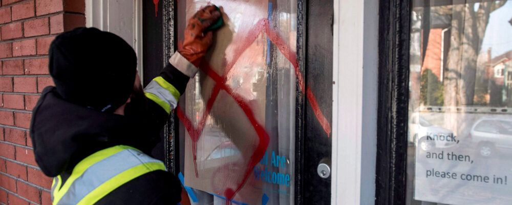 A graffiti removal worker cleans anti-Semitic graffiti, including a swastika, that was spray painted on the door of The Glebe Minyan and home of Rabbi Anna Maranta, on Tuesday, Nov. 15, 2016 in Ottawa. Justin Tang/The Canadian Press. 