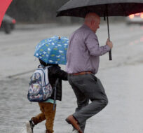 As the rain falls, a father walks his son to Garfield Elementary through a flooded section of Peach and Need Avenues, on Monday, Oct. 25, 2021, in Clovis, Calif. John Walker/The Fresno Bee via AP.