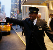 Veteran doorman Thales Cadet, who claims, "the world comes to me everyday," hails a cab in front of the Waldorf-Astoria hotel, Tuesday, Feb. 28, 2017, in New York. Kathy Willens/AP Photo. 