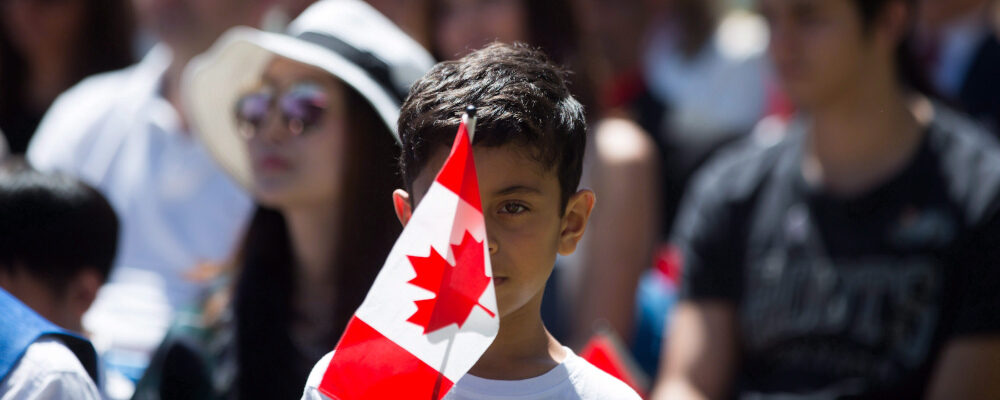A young boy holds a Canadian flag while watching a special Canada Day citizenship ceremony in West Vancouver, B.C., on Saturday, July 1, 2017. Darryl Dyck/The Canadian Press. 
