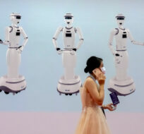 An attendee uses her smartphone as she walks past a mural showing service robots at the World Robot Conference in Beijing, Saturday, Sept. 11, 2021. Mark Schiefelbein/AP Photo.