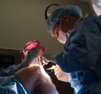 Dr. Darius Viskontas, right, with assistance from Dr. Anne Wachsmuth, removes a cyst from a male patient's knee at the Cambie Surgery Centre, in Vancouver on Wednesday, August 31, 2016. Darryl Dyck/The Canadian Press. 