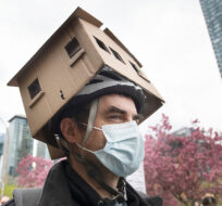 A man wears a cardboard house on his head during a demonstration calling for more affordable and social housing in Montreal, Saturday, May 8, 2021. Graham Hughes/The Canadian Press. 