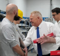 Ontario Premier Doug Ford, centre, and Ontario Finance Minister Peter Bethlenfalvy, right, walk in with doughnuts and greet trades people before painting a mock-up wall during a pre-budget photo opportunity at the International Union of Painters' Allied Trades facility in Toronto on Thursday, March 23, 2023. Nathan Denette/The Canadian Press. 