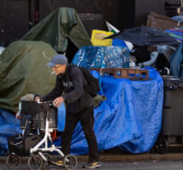 A man using a rolling walker walks on the street past tents setup on the sidewalk at a sprawling homeless encampment on East Hastings Street in the Downtown Eastside of Vancouver, on Tuesday, August 16, 2022. Darryl Dyck/The Canadian Press. 