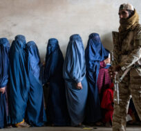 A Taliban fighter stands guard as women wait to receive food rations distributed by a humanitarian aid group, in Kabul, Afghanistan, Tuesday, May 23, 2023. Ebrahim Noroozi/AP Photo.