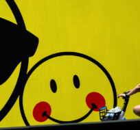 A woman rides a bicycle past a smiley faces billboard outside a shopping mall in Beijing, Monday, July 19, 2021. Andy Wong/AP Photo. 