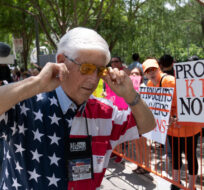 A member of the National Rifle Association plugs his ears with his fingers as he walks past protesters during the NRA Annual Meetings Exhibits at the George R. Brown Convention Center, May 27, 2022, in Houston. Jae C. Hong/AP Photo.