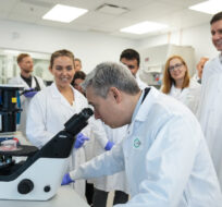 Francois-Philippe Champagne, Federal Minister of Innovation, Science and Industry, looks through a microscope as research scientist Elodie Da Costa, back left, and B.C. Premier David Eby, back right, watch during a tour of a lab at AbCellera, in Vancouver, on Wednesday, May 24, 2023. Darryl Dyck/The Canadian Press. 