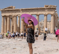 A woman takes a selfie in front of Parthenon temple atop of the ancient Acropolis hill during a heat wave in Athens, Greece, Friday, July 21, 2023. Petros Giannakouris/AP Photo. 