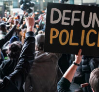 In this Oct. 14, 2020, file photo a protester holds a sign that reads "Defund Police" during a rally for the late George Floyd outside Barclays Center in New York. John Minchillo/AP Photo. 