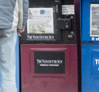 A man looks at newspaper boxes containing the Vancouver Sun and the Province in downtown Vancouver on Jan. 19, 2016. Jonathan Hayward/The Canadian Press.