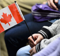 A young new Canadian holds a flag as she takes part in a citizenship ceremony on Parliament Hill in Ottawa on April 17, 2019. Sean Kilpatrick/The Canadian Press.