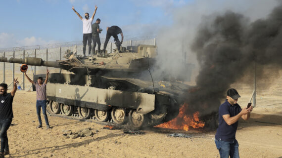 Palestinians celebrate by a destroyed Israeli tank at the Gaza Strip fence east of Khan Younis on Oct. 7, 2023. Hassan Eslaiah/AP Photo.